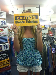 a woman holding up a sign in front of her face that says caution blonde thinking