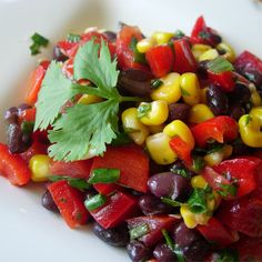 a white plate topped with corn, black beans and cilantros on top of green garnish