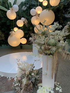 two white vases with flowers and paper lanterns hanging from the ceiling in front of them