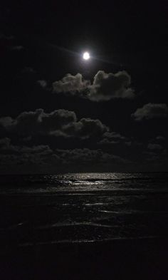 the moon is shining over the ocean at night with clouds in the sky and dark water