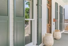 two large vases sitting on the front porch of a house with green shutters