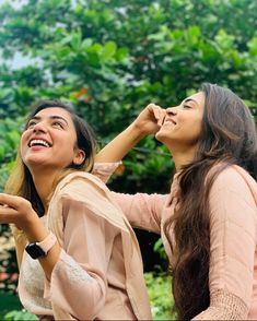 two women standing next to each other and looking up at something in the air with trees behind them