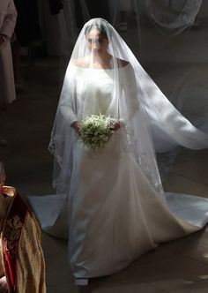 the bride is walking down the aisle with her veil on and flowers in her hand