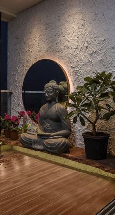 a buddha statue sitting on top of a wooden floor next to a potted plant