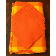 six orange napkins sitting on top of a wooden table next to an orange and yellow checkered cloth