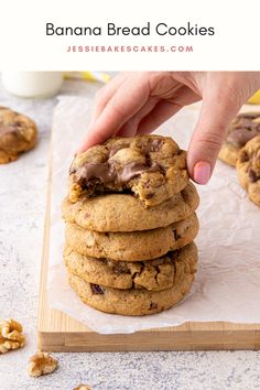 a hand picking up a chocolate chip cookie from a stack on top of parchment paper