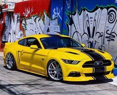 a yellow ford mustang parked in front of graffiti covered wall with black and white stripes