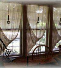 two chairs are sitting in front of three windows with sheer curtains hanging from the ceiling