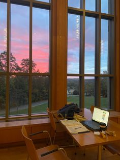 a laptop computer sitting on top of a wooden desk in front of large glass windows