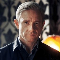 a man with grey hair and blue shirt looking at the camera while standing in front of a wall