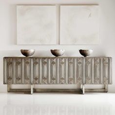 three silver bowls sitting on top of a metal cabinet in front of two pictures hanging on the wall