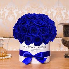 a blue rose bouquet in a white box on a table next to other vases