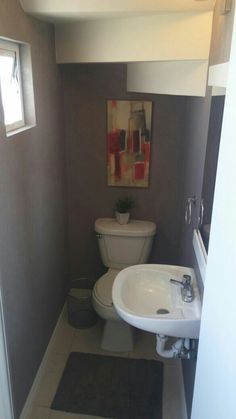 a white toilet sitting next to a sink in a bathroom under a painting on the wall