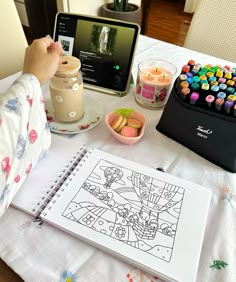 a person sitting at a table in front of a laptop computer with a coloring book on it