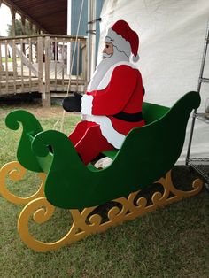 a santa clause sitting in a sleigh on the grass next to a tent