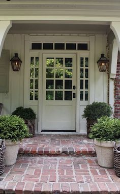 the front door is open and there are plants in pots on the brick walkway outside