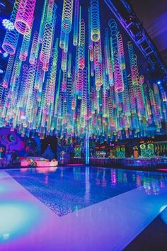 an indoor dance floor is lit up with multicolored lights and chandeliers