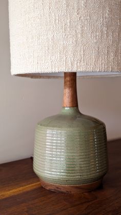 a green lamp sitting on top of a wooden table next to a white light shade