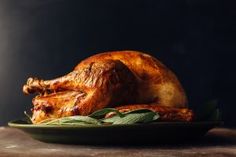 a roasted turkey on a green plate with sage leaves in the foreground and dark background