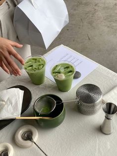 two cups of green tea on a table with napkins and spoons next to it