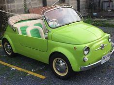 an old green car is parked in a parking lot next to a brick wall and fence