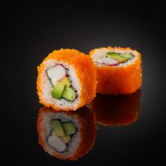 two pieces of sushi with cucumber and avocado on black background