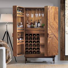 an armoire with wine glasses and bottles in it is next to a couch that has a rug on the floor