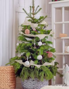 a small christmas tree in a basket with ornaments on the top and ribbon around it