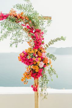 an arrangement of colorful flowers on top of a wooden pole with water in the background