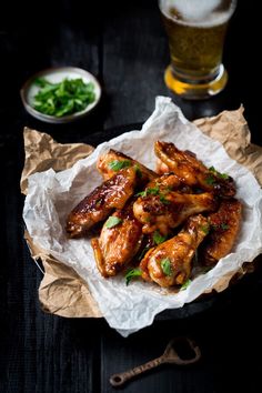 chicken wings with herbs and sauce on a paper wrapper next to a glass of beer