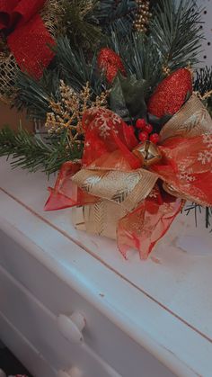 a close up of a christmas decoration on a white dresser with red and gold bows