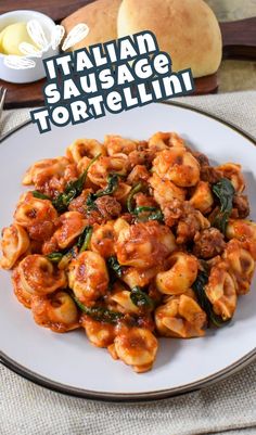 pasta with sausage and spinach in tomato sauce on a white plate next to bread