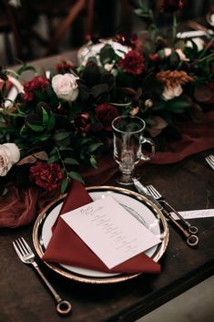 a place setting with red napkins, silverware and flowers on a wooden table