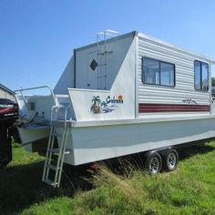 a white boat sitting on top of a lush green field next to a motor home