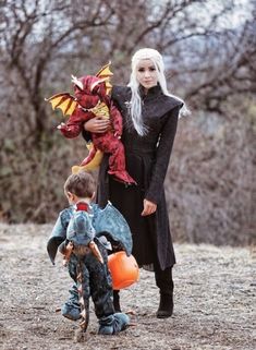 a woman in black dress holding a dragon toy and standing next to a little boy