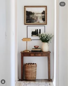 a hallway with a table, lamp and pictures on the wall above it is shown