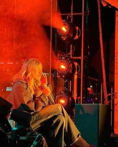 a woman sitting on top of a chair in front of a stage with red lights