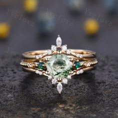 a green and white diamond ring sitting on top of a black stone surface with gold band