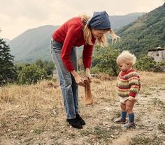 a woman holding a shovel next to a toddler on top of a dirt field