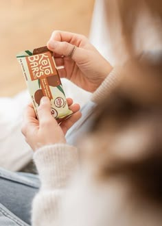 a woman is holding a chocolate bar in her hand while sitting on the floor and looking at it