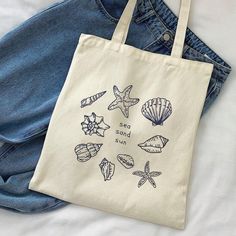 This fabric bag "from the sea" is the perfect beach tote bag option for this summer. It has a minimalist but stylish design that will elevate your outfit to the next level. It is an ideal gift for bachelorette parties, for the birthday of your friend who loves the sea, for your sister and, in short, a tote bag for everyone. The size is ideal to use as a day-to-day bag, as a bag for the beach or for shopping. In addition, it is very comfortable because its handles are long and can fit many things Tote Bag Summer Design, Tote Bag Painting Ideas Beach, Painted Canvas Tote Bags, Cute Tote Bag Ideas, Tote Bag Ideas Design, Creative Tote Bag Design Ideas, Summer Tote Bag Design, Tote Bag Decorating Ideas