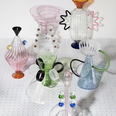 several different colored glass vases sitting on top of a white tableclothed surface