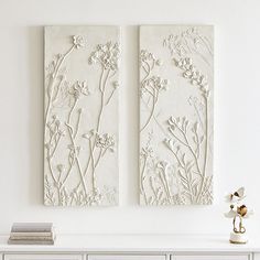 two white flowers are on the wall next to each other in front of a dresser