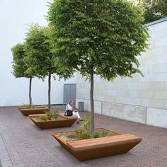 a woman sitting on a bench under a tree in a courtyard with several planters