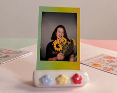 a photo frame with flowers in it sitting on a table next to two video game controllers