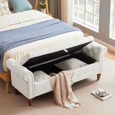 a white bed with an open storage compartment underneath it on the floor next to a window