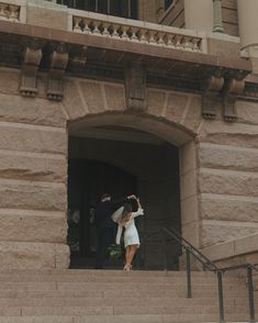 a man and woman standing on the steps of a building with their arms in the air