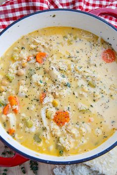 a bowl of chicken and dumpling soup on a red checkered table cloth next to bread