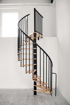 a spiral staircase in an empty room with white walls and wood flooring on the side