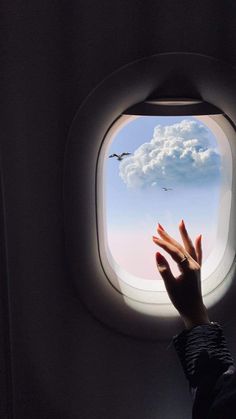 a person reaching out an airplane window at the sky with clouds and birds flying overhead